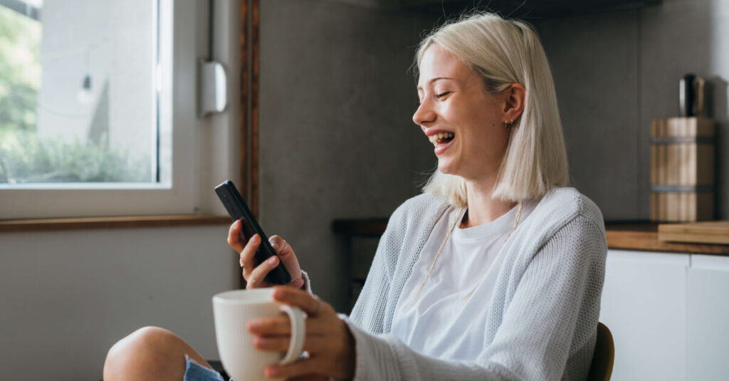 Person on their phone laughing while drinking coffee